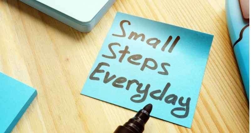 A blue sticky note with the handwritten phrase “Small Steps Everyday” is placed on a wooden desk, highlighting the importance of consistent progress in daily rituals.