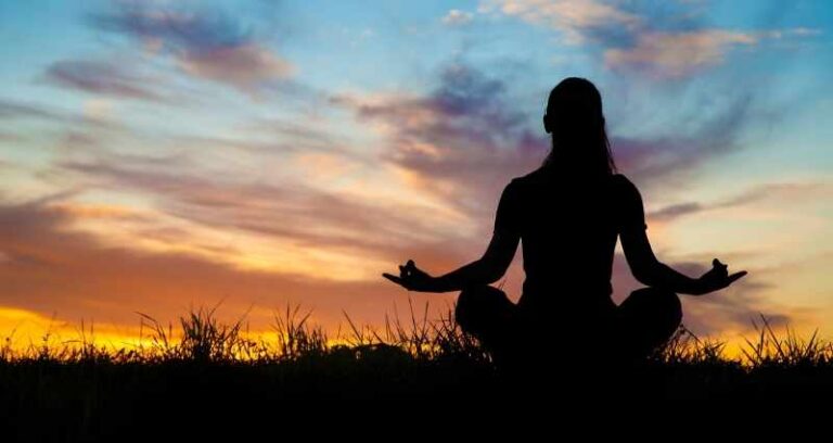 A silhouette of a person meditating at sunrise in a serene outdoor setting, symbolizing inner peace and focus.