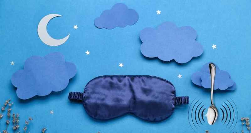 A blue sleep mask lies on a backdrop of paper clouds, stars, and a crescent moon, with a spoon balanced upright beside it. This image symbolizes creative methods, such as using the hypnagogic state—the transitional phase between wakefulness and sleep—to access subconscious insights and spark innovative ideas.