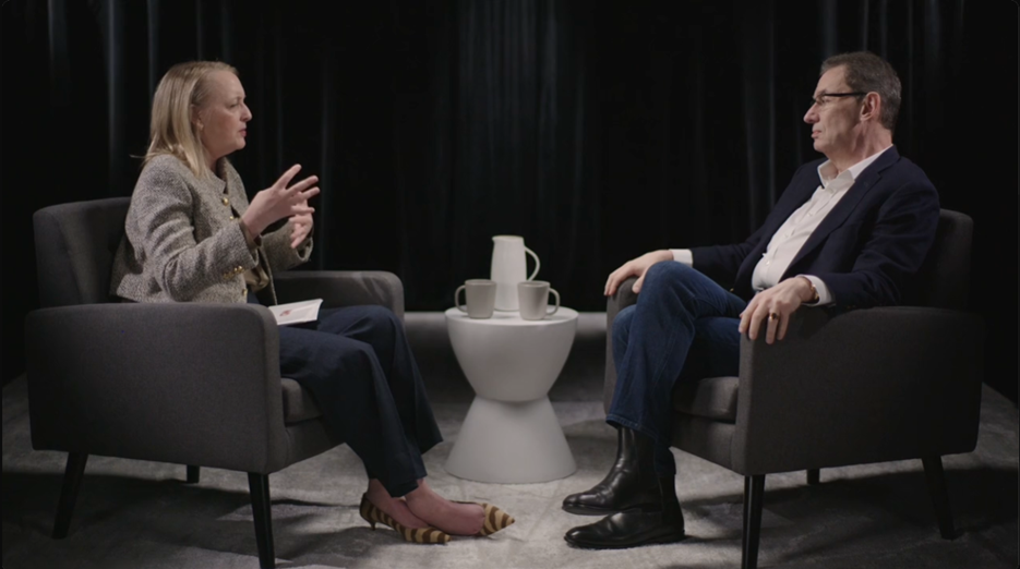 CNN-style executive interview with two CEOs discussing business topics in a studio setting with chairs, table, and coffee cups.