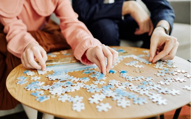 Hands placing puzzle pieces into a puzzle